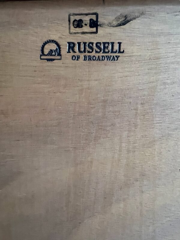 Enfilade conçue par WH Russell pour Russells of Broadway dans les années 1950'. Le buffet est composé d'une section centrale de trois tiroirs flanqués assemblés en queue d'aronde, d'une porte de placard sur chaque extrémité dont une est munie d'une étagère. Les tiroirs sont habillés de poignées circulaires en bois. Le buffet est fabriqué en noyer avec un mélange de placages et de bois massif reposant sur des pieds fuselés chanfreinés en hêtre. Pièce rare fabriqué à la main portant l'estampille du fabricant à l'arrière du meuble.